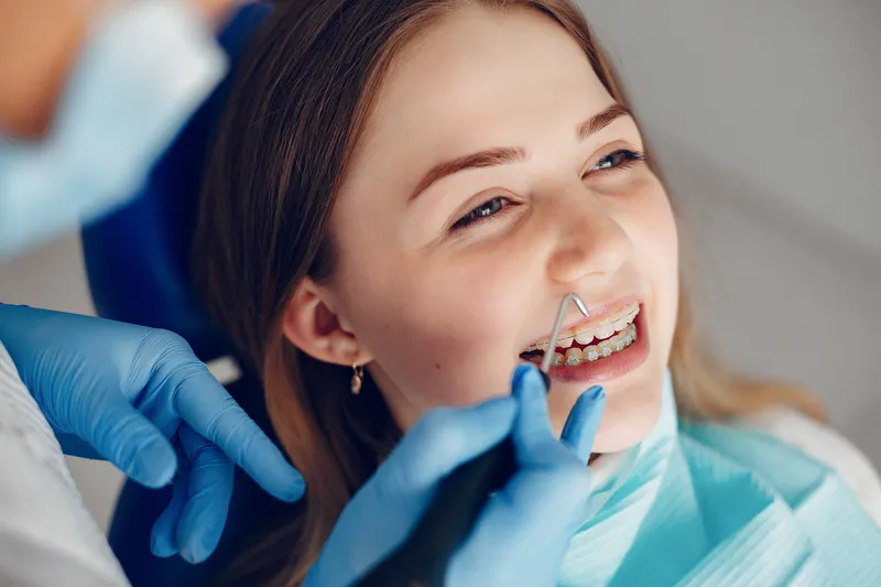 Paciente sonriendo durante una revisión dental con brackets mientras el especialista realiza el tratamiento.